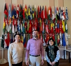 Three people standing in front of the flag wall at the IACA Campus.